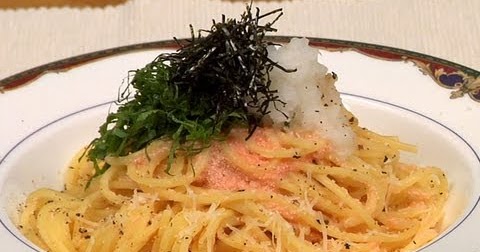 This is a color photograph showing a plate of Japanese-style pasta or noodles. The image shows a white plate with a decorative rim containing what appears to be spaghetti or thin noodles garnished with dark seaweed (likely nori), green herbs or scallions, a white component (possibly grated daikon radish or cheese), and what looks like sliced fish or meat with a pink/red coloring. The dish represents a fusion of Italian pasta with Japanese ingredients and presentation style. The photo is taken...